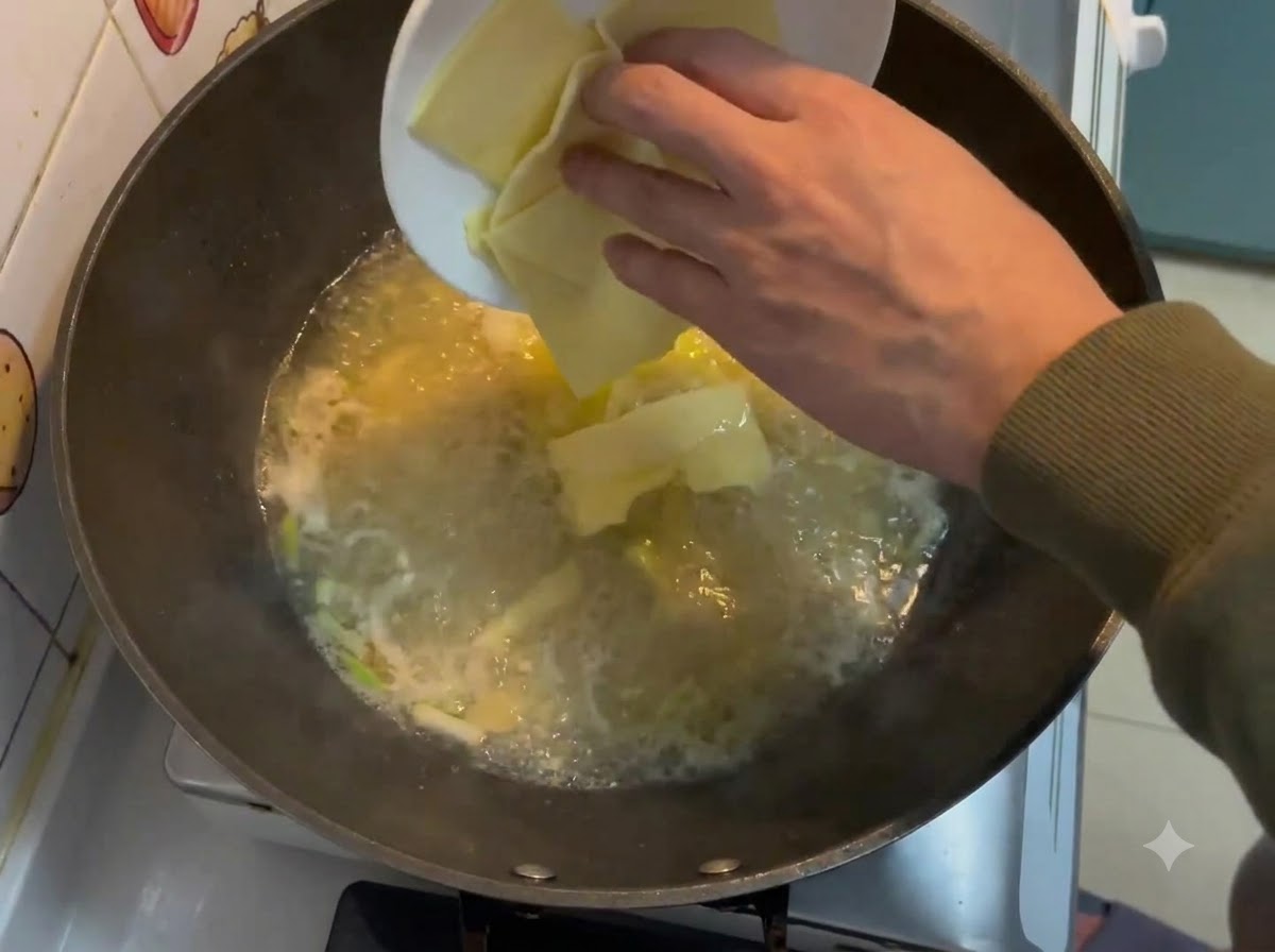 Square cheese slices being dropped from a white plate into a bubbling creamy broth in a wok.