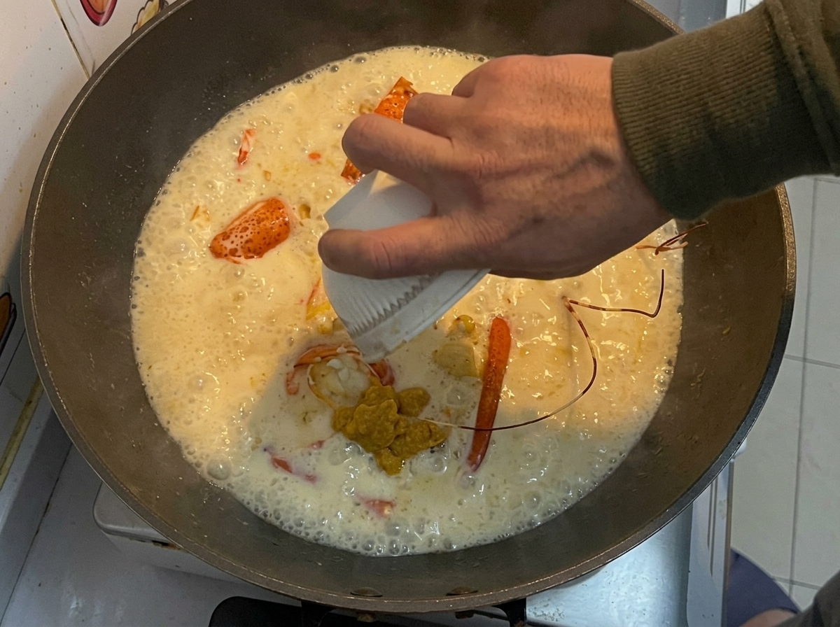 The reserved yellow lobster paste being poured from a small white bowl into a wok with fried lobster pieces and a creamy sauce.