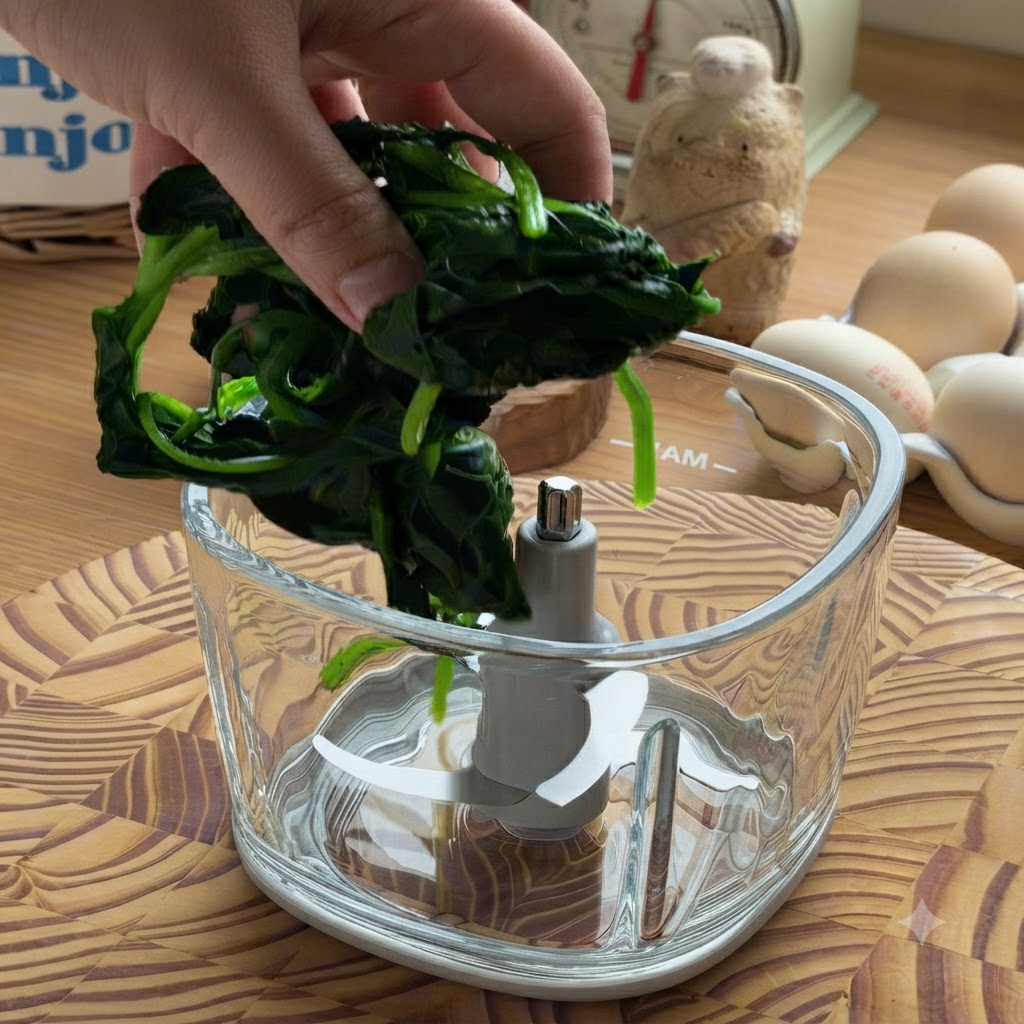 A hand placing a clump of squeezed, cooked spinach into an empty glass food processor bowl.