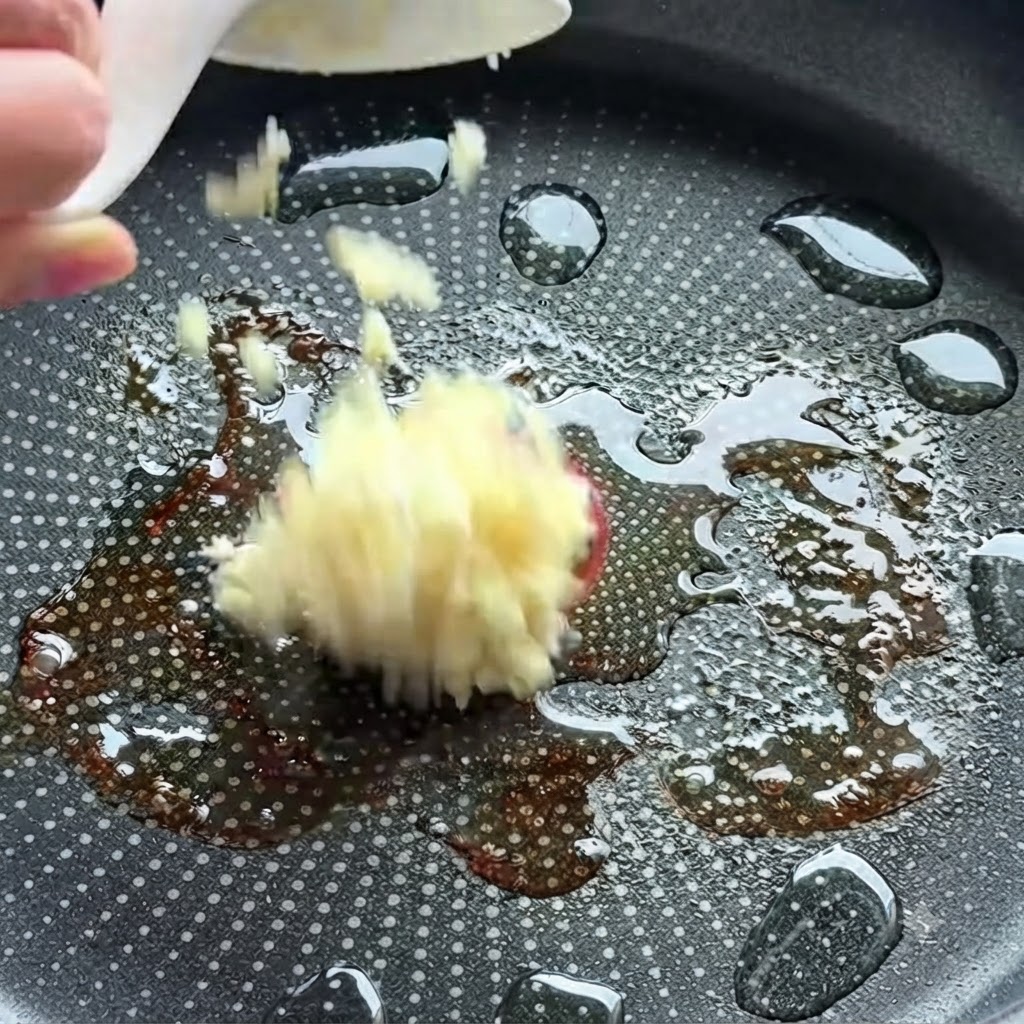 Minced garlic being dropped into a hot frying pan with oil.