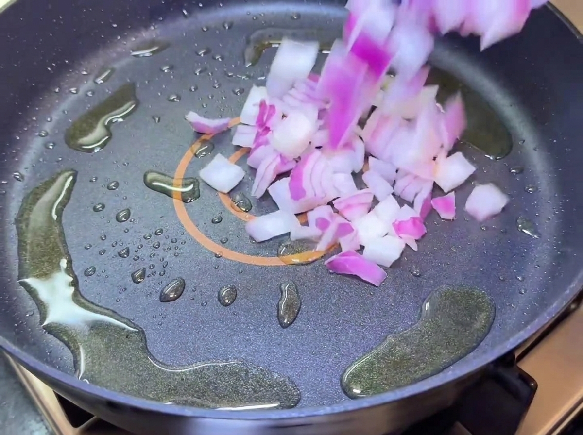 Diced red onions falling into a frying pan with oil.