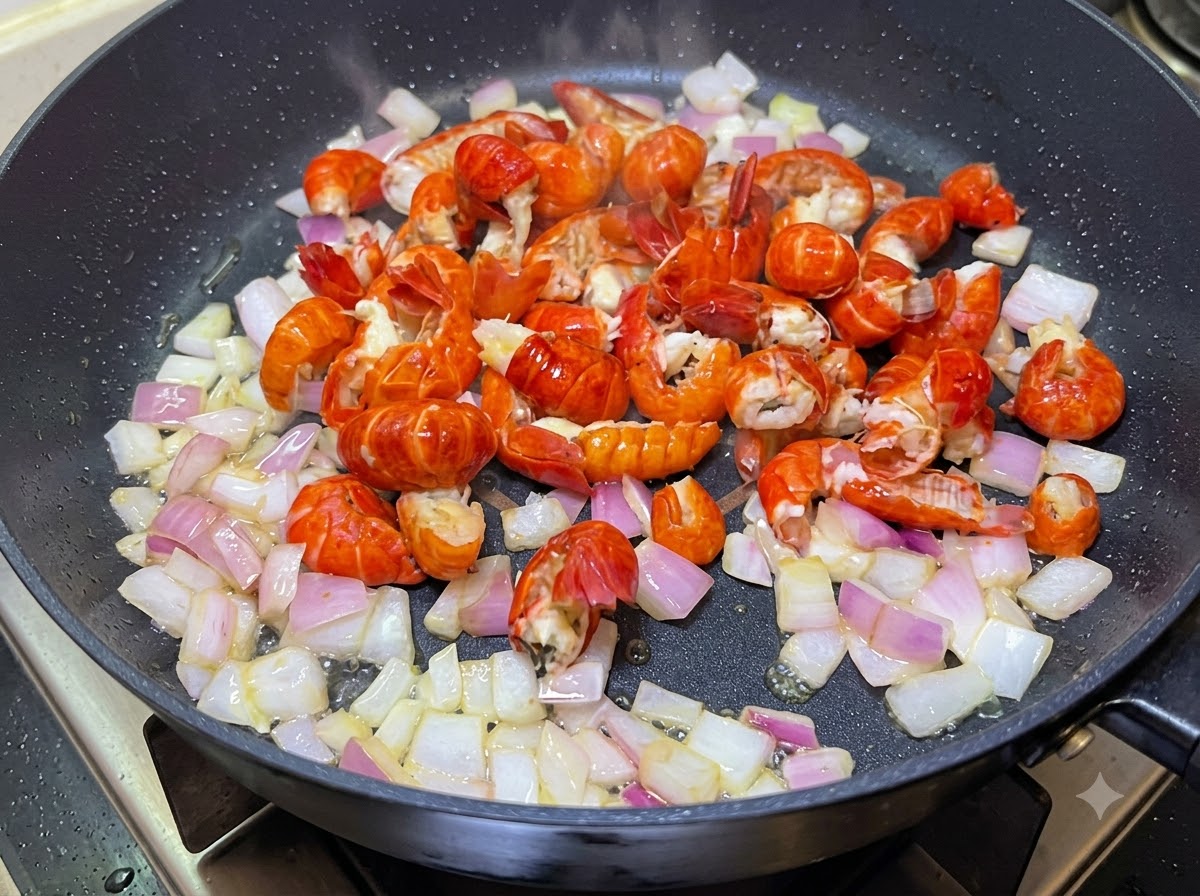 Crayfish tails and diced onions being cooked together in a pan.