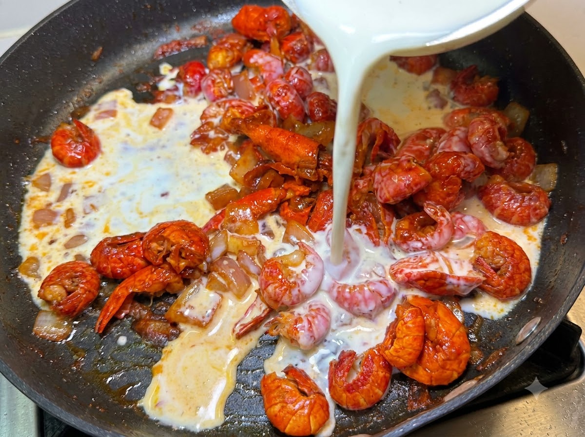 Milk and whipping cream being poured from a bowl into the pan containing crayfish and onions.