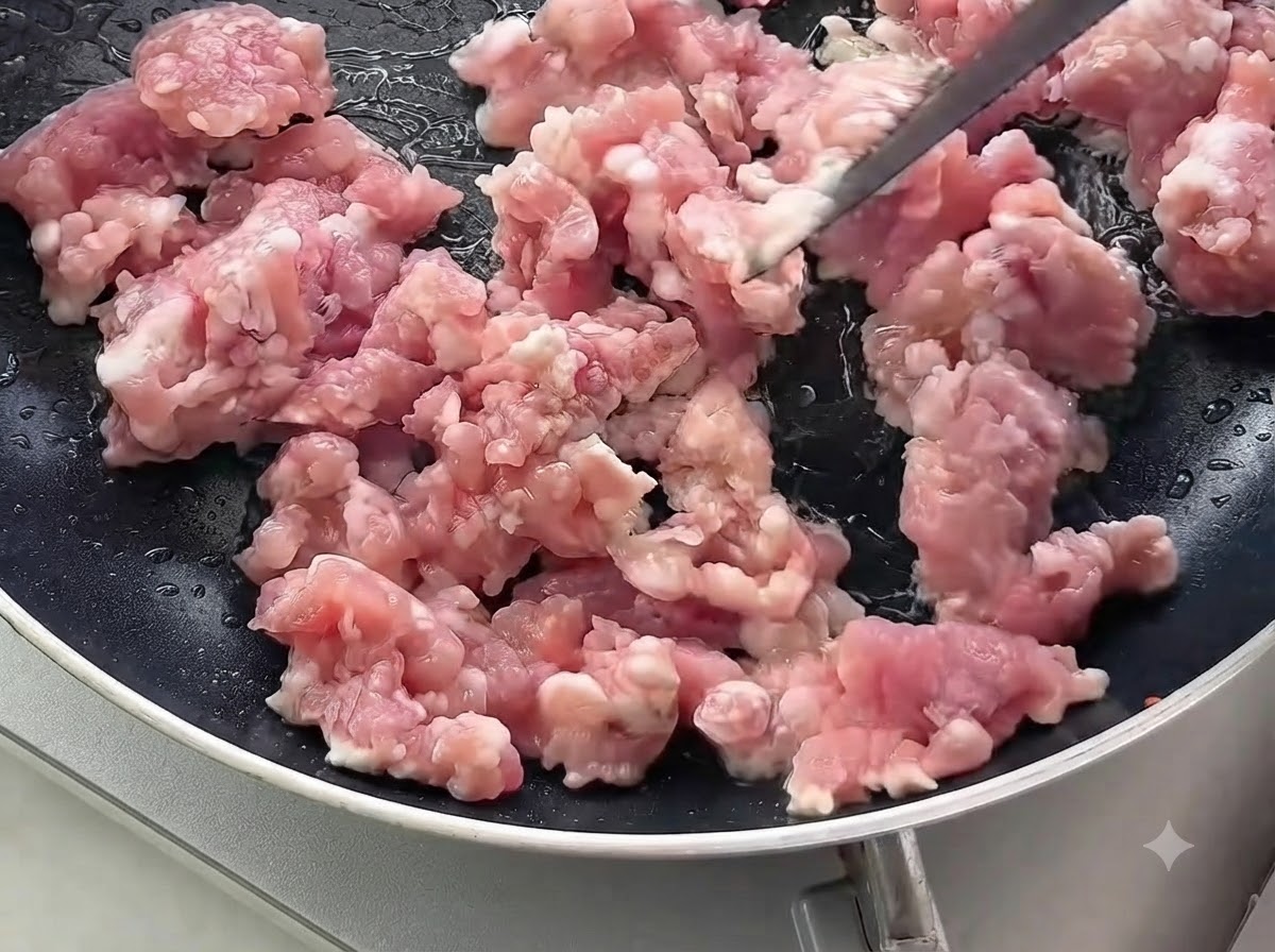 Raw minced pork being stirred and cooked in a black frying pan.