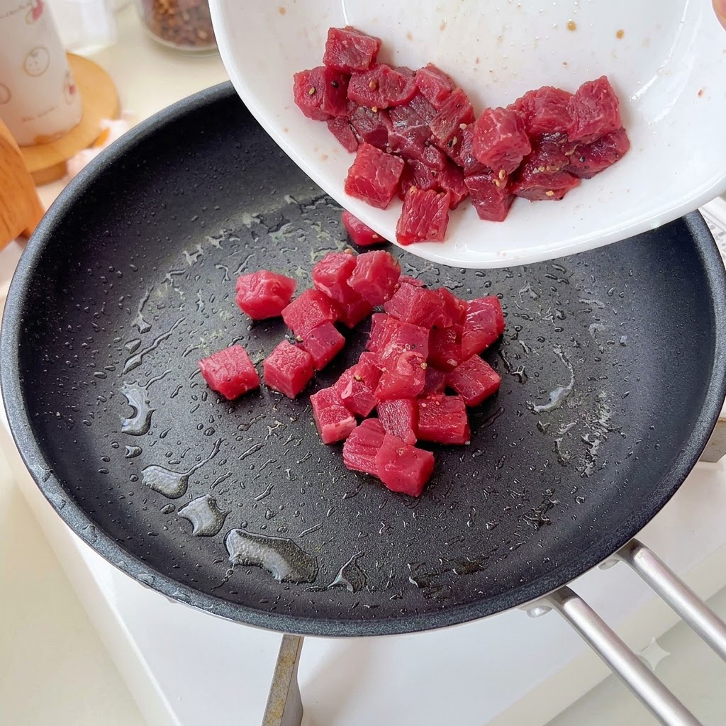 Seasoned beef cubes being poured and stir-fried in a pan.