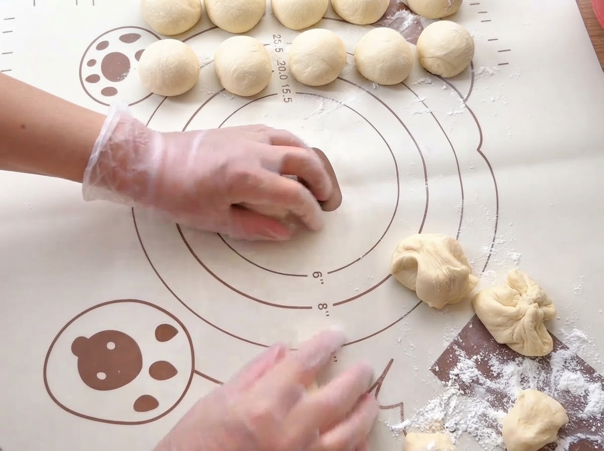 Hands rolling small portions of dough into smooth balls on a printed silicone baking mat.