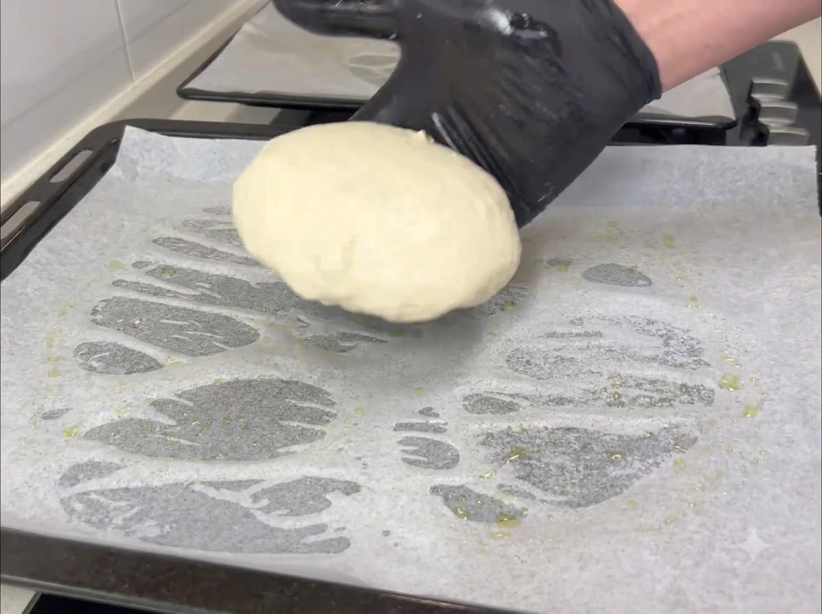 A gloved hand transferring a small round portion of dough onto a parchment-paper-lined baking sheet.