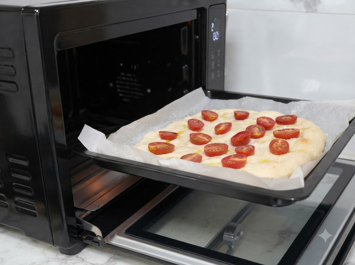 A baking tray with topped pizza dough being slid into a black oven.