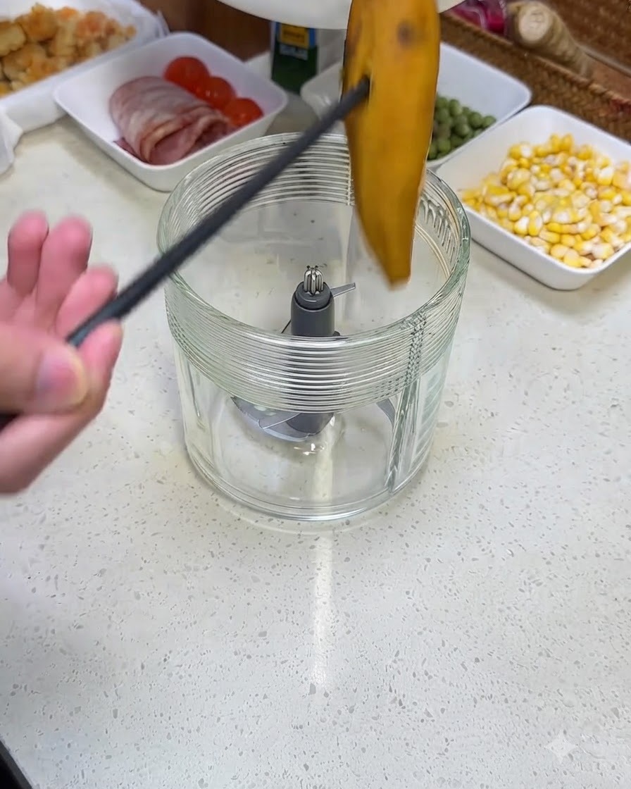 A person using black tongs to drop a cooked sweet potato into a glass blender jar.