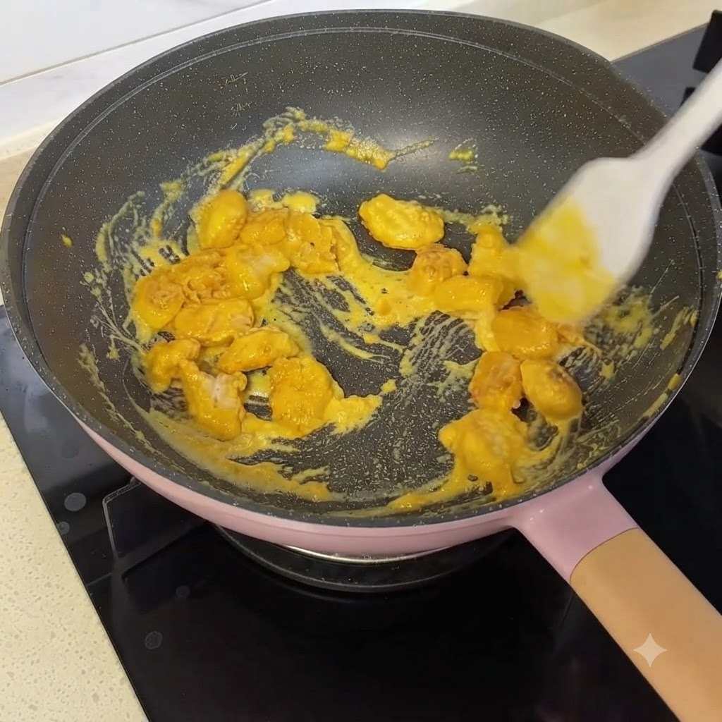 Popcorn chicken pieces being stirred and coated with yellow salted egg yolk sauce in a pan using a silicone spatula.