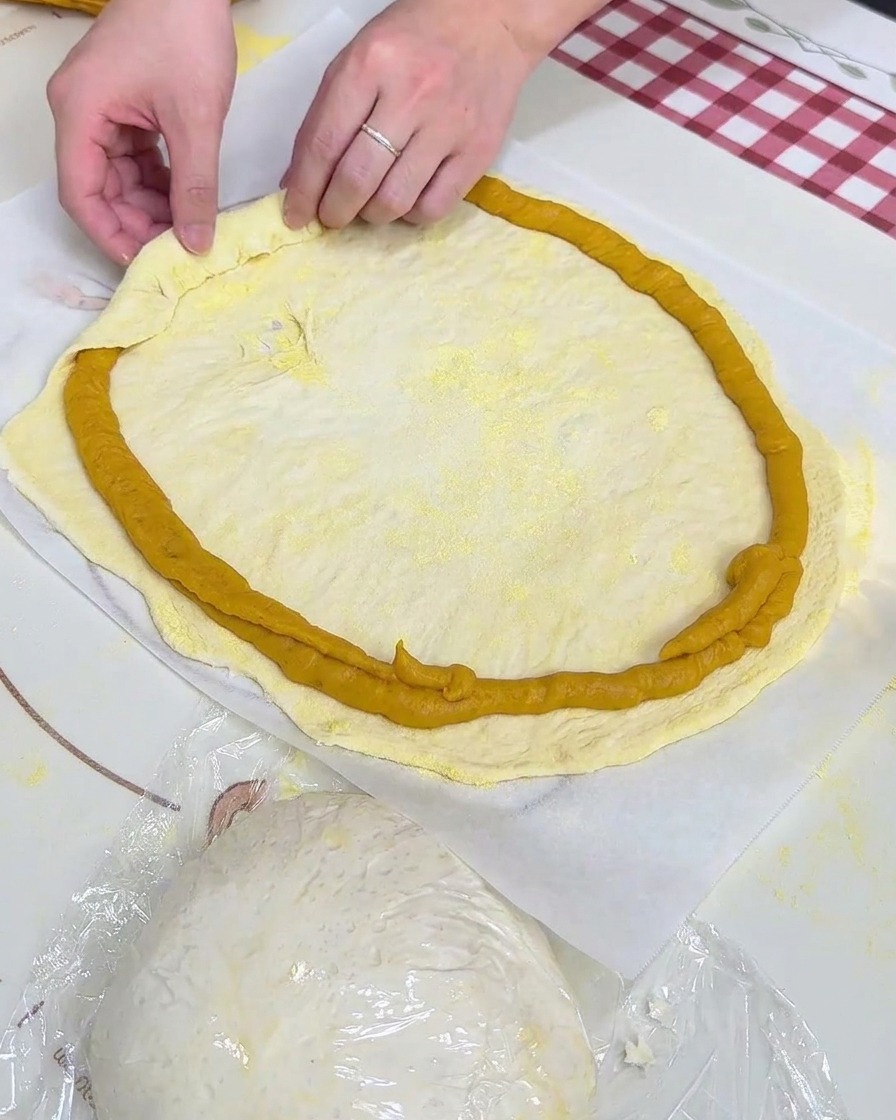 Hands folding the dough border over the piped sweet potato mash ring on parchment paper.