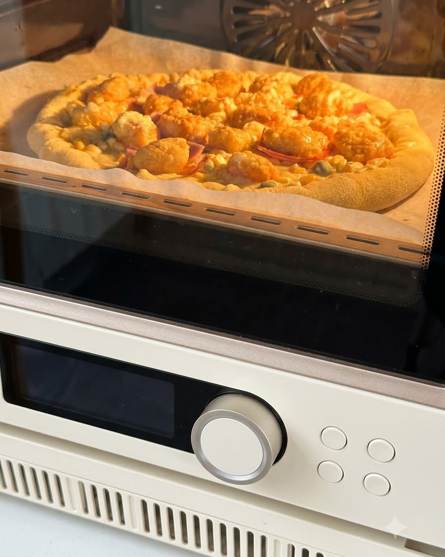 Assembled pizza on parchment paper being placed inside an oven to bake with the interior glowing warm orange.