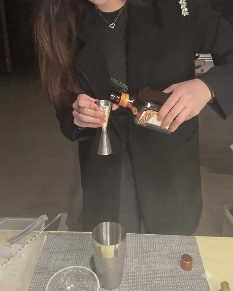 Cointreau being poured into a jigger with a shaker tin below.