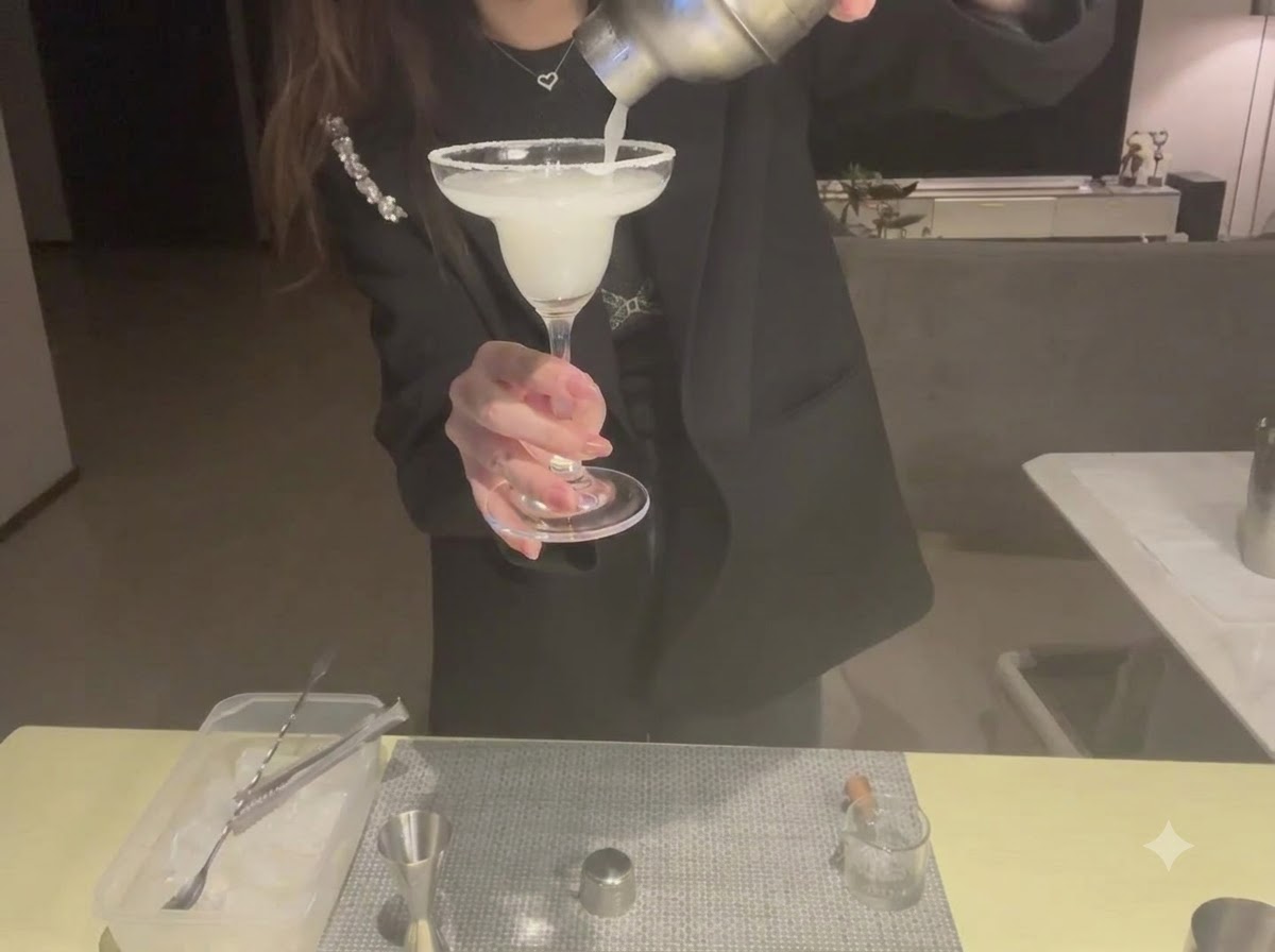 A close-up of a lemon slice being carefully mounted onto the rim of a margarita glass.