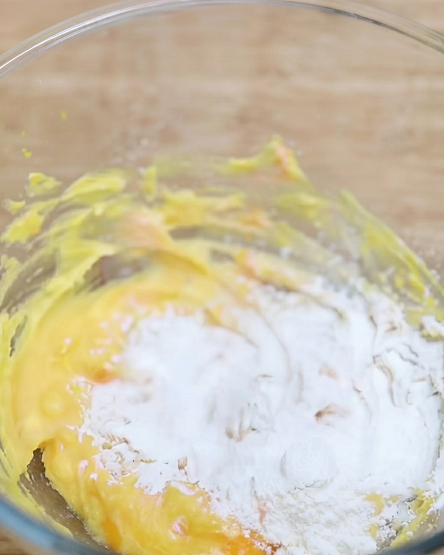 Matcha powder being sifted into a bowl containing the yellow dough base.