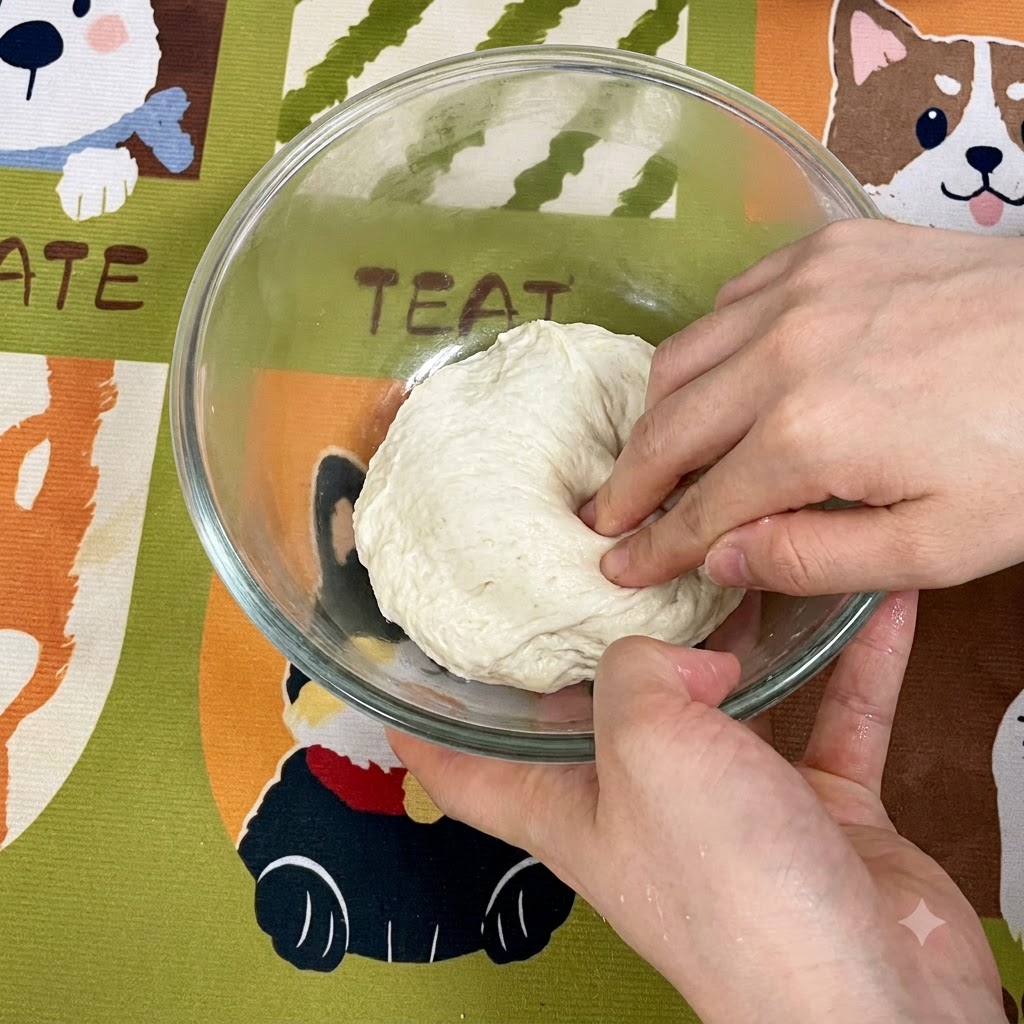 Hands stretching and folding the sticky dough toward the middle inside a glass bowl.