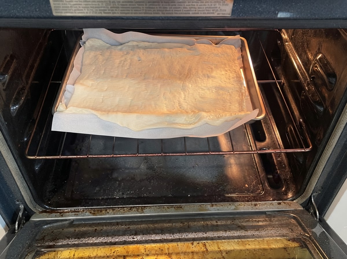 A baking sheet with raw pizza dough on parchment paper placed on the oven rack inside a preheated oven.
