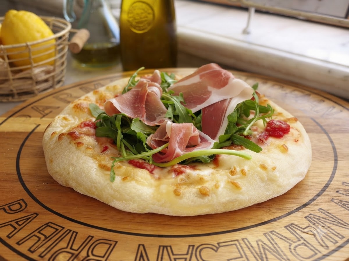 Freshly shaved Parmesan cheese falling onto a prepared pizza topped with greens and cured meat.