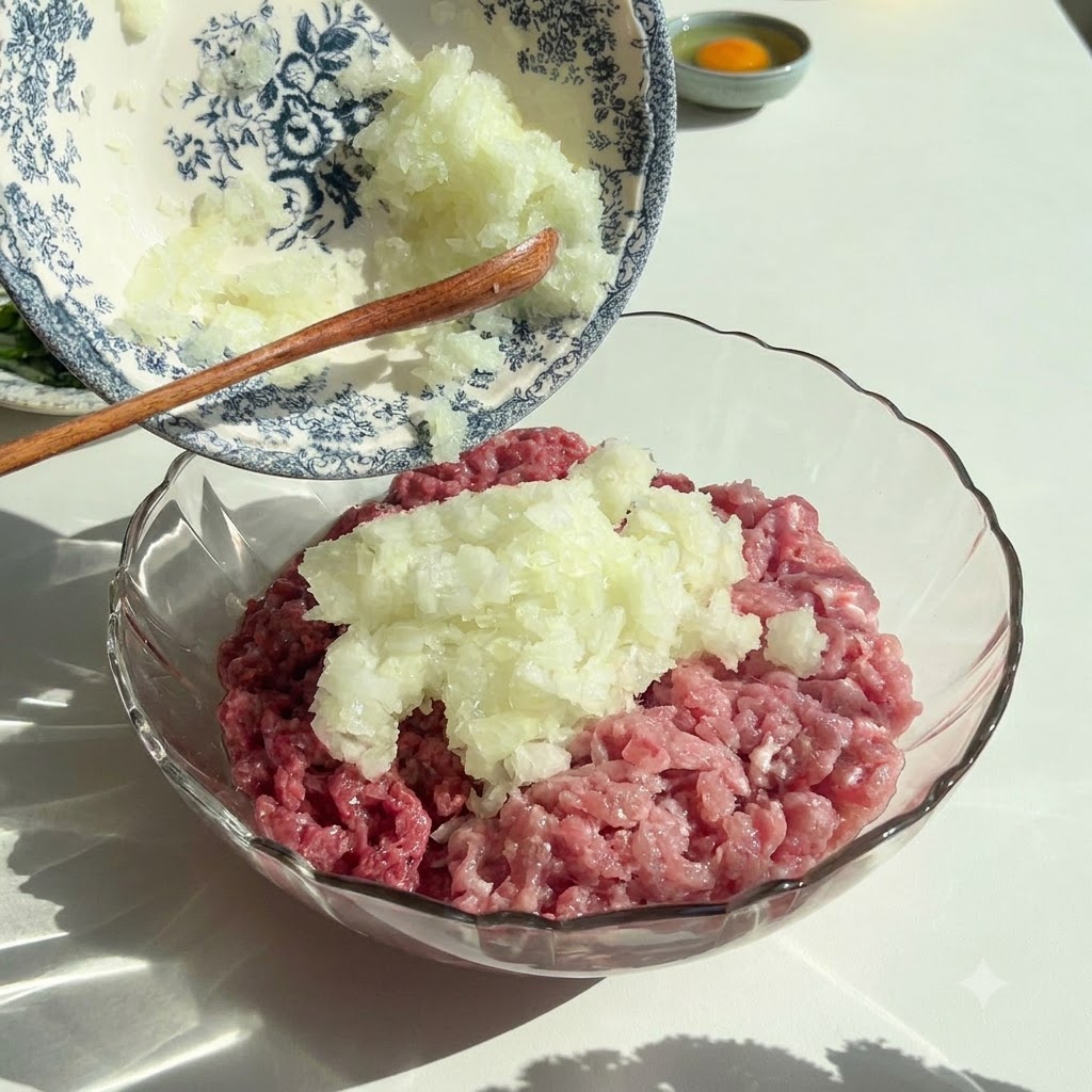 Finely chopped onions and parsley being poured from a decorative bowl into a glass bowl containing raw ground meat.