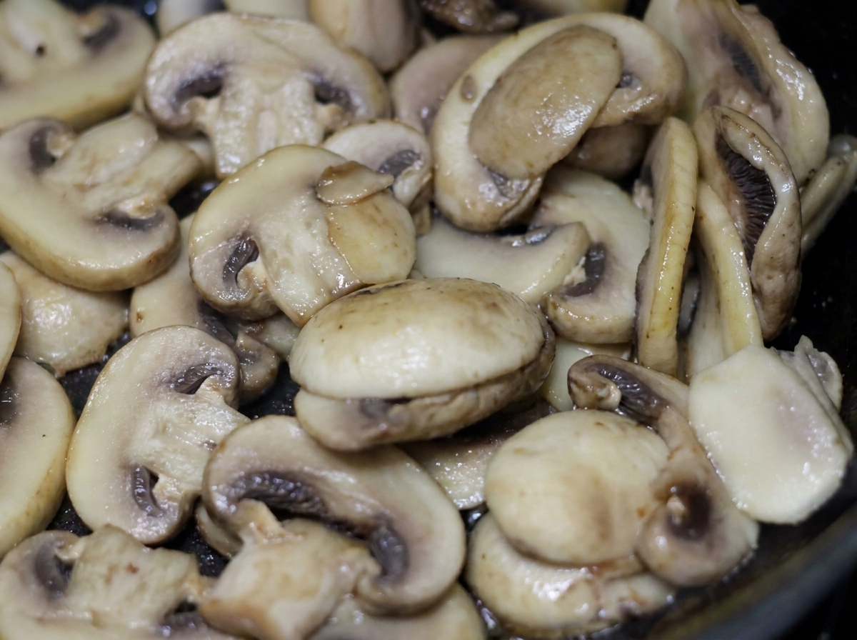 Sliced white button mushrooms sizzling and cooking in a pan with light cream.