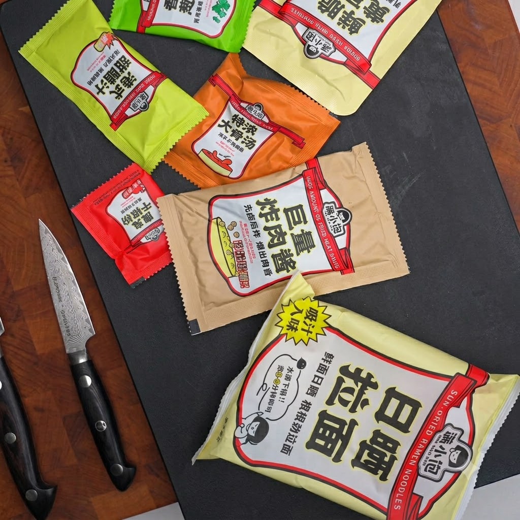Various seasoning packets, sauce sachets, and a knife laid out on a dark surface.
