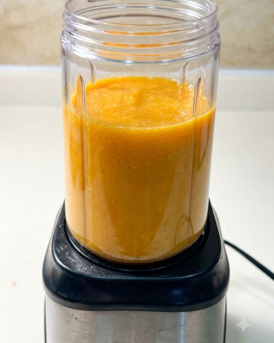 A blender cup filled with an orange soup mixture sitting on top of a black blender motor base.
