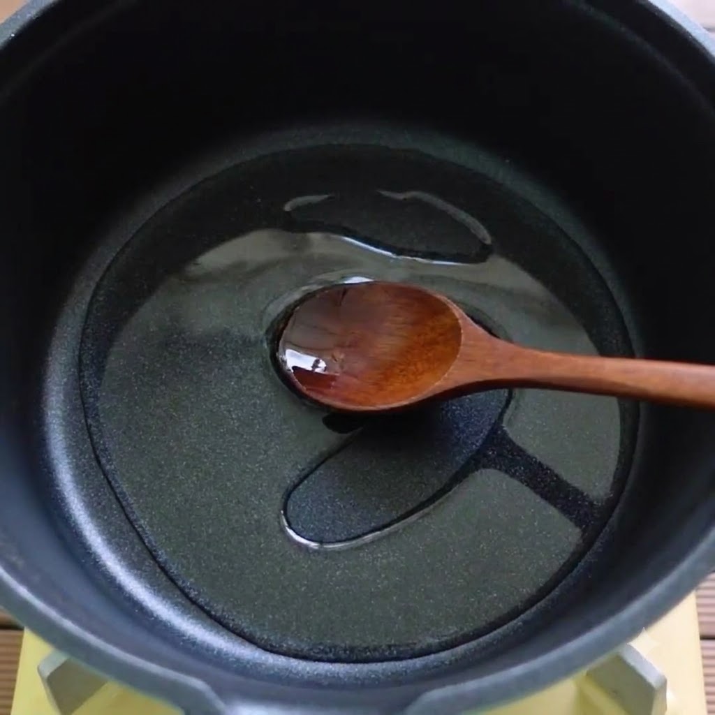 A wooden spoon stirring oil and melted ingredients in a black pot.
