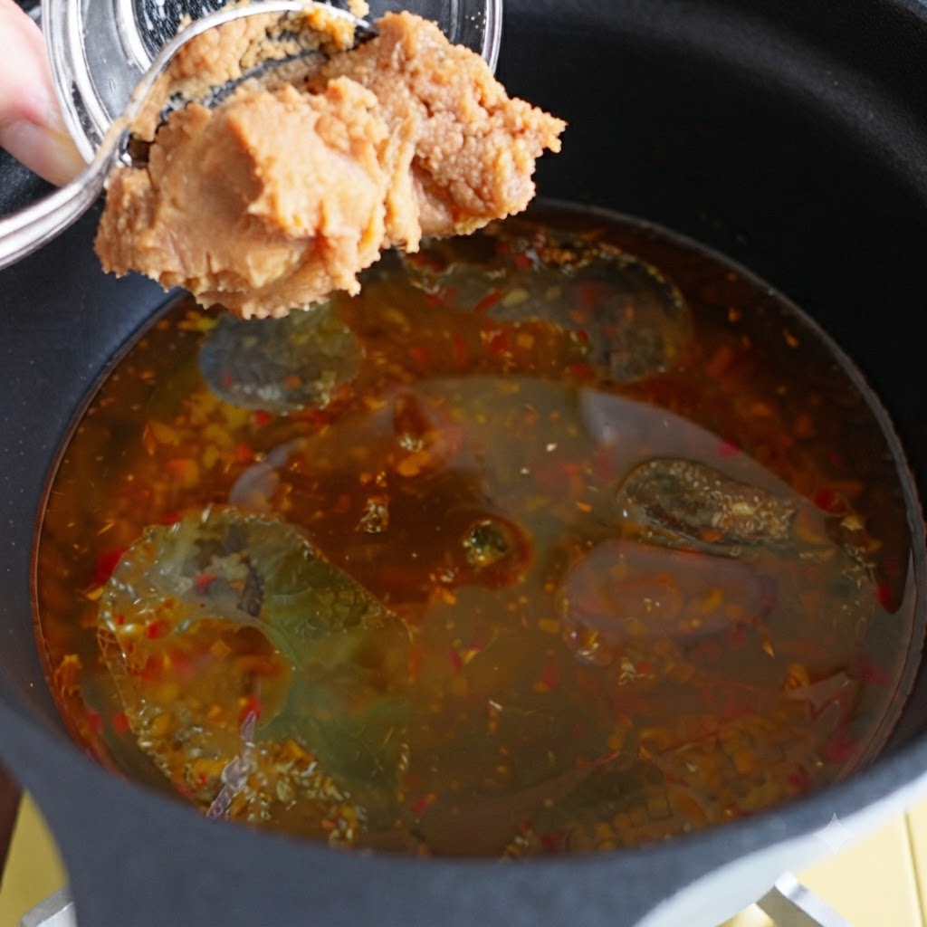 Miso paste being added into a pot of seasoned broth.