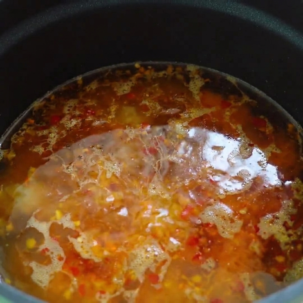 Chili oil and sesame oil being drizzled across the surface of the hot soup base.