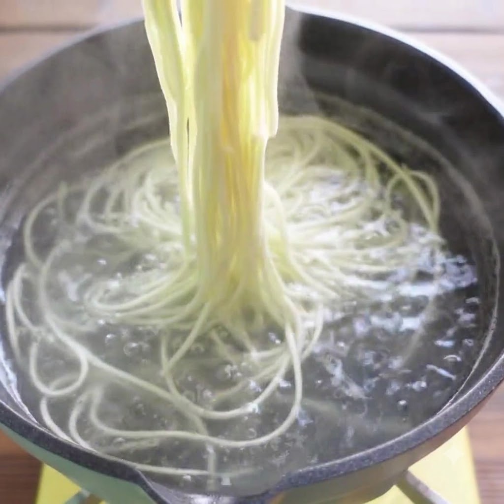 Chopsticks lifting cooked ramen noodles out of boiling water.