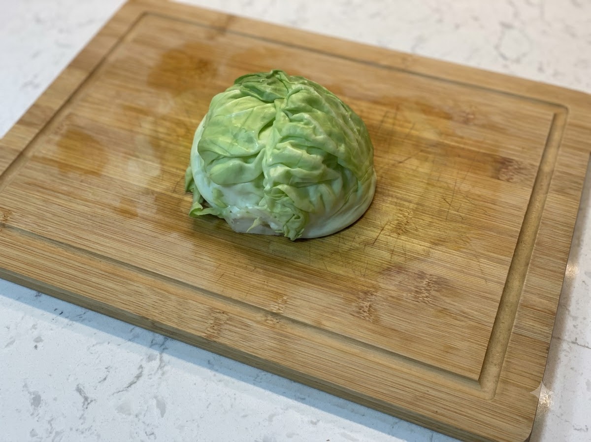 A wedge of fresh green cabbage resting on a wooden cutting board.