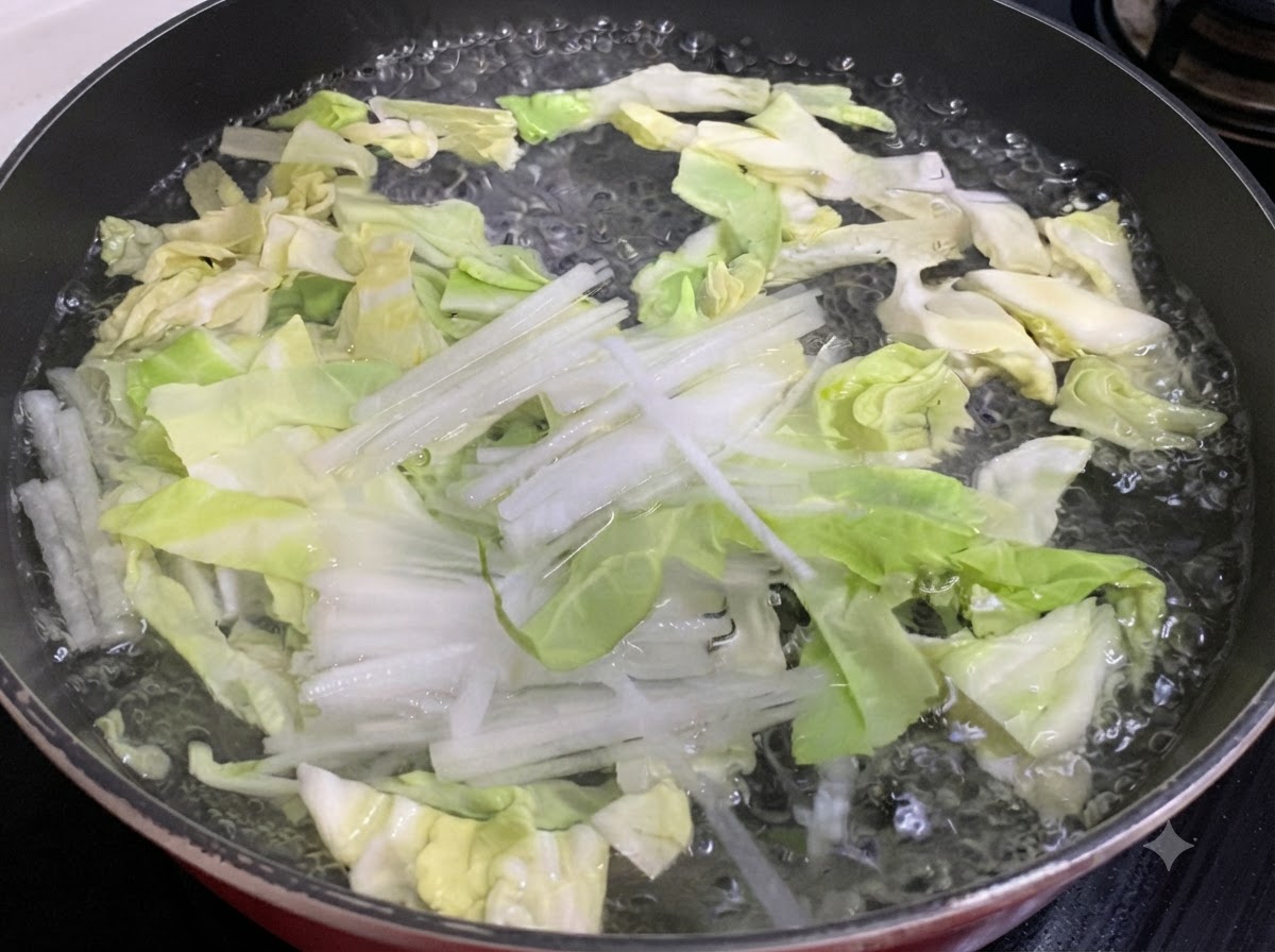 Shredded cabbage and white radish boiling in a pan of water.