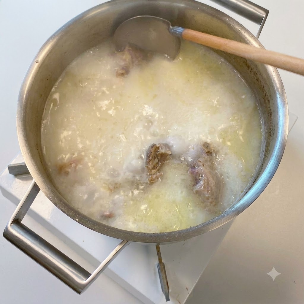 A wooden ladle dipping into a pot of opaque, milky white simmering pork bone broth.