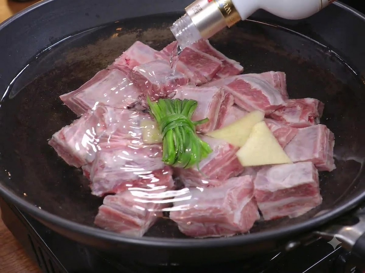 Steak pieces being placed into a pot of water with green onions and ginger for blanching.