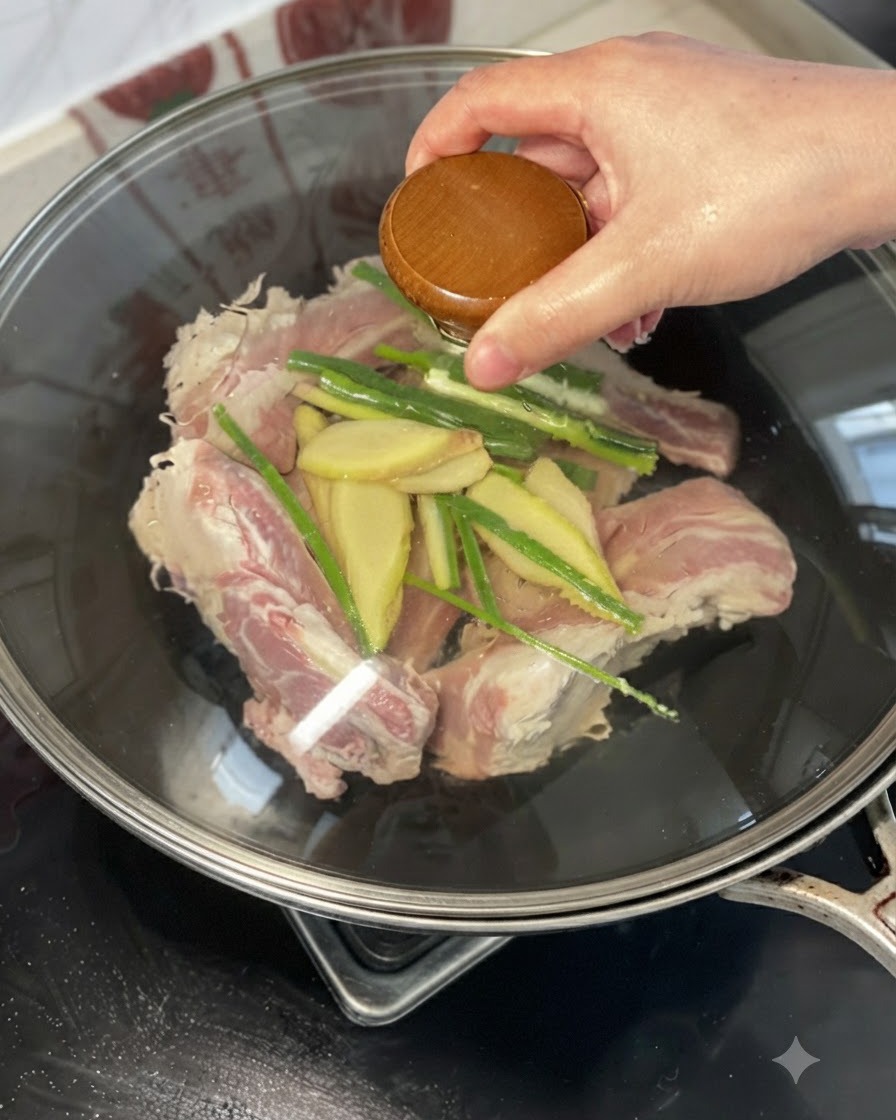 A hand holding a lid or pouring yellow wine over beef ribs, ginger, and green onions in a wok.