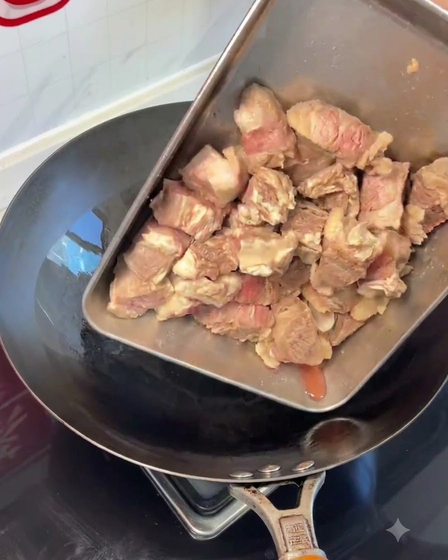 Blanched beef rib pieces being poured from a steel tray into a hot wok.