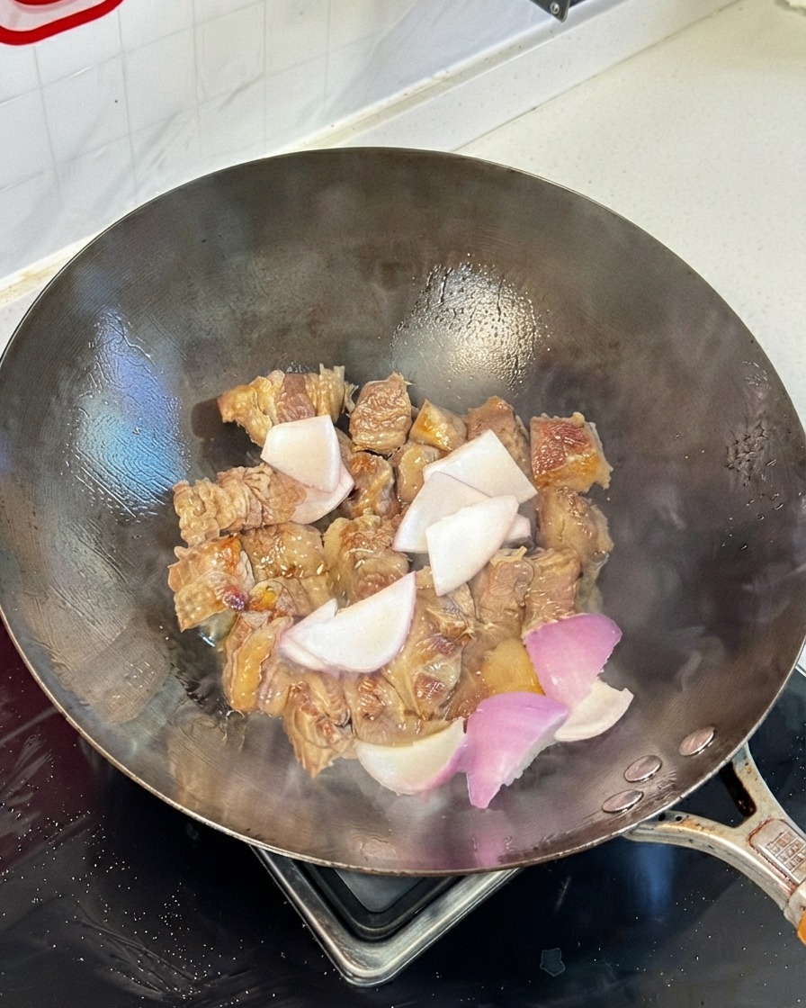 Stir-fried beef rib pieces in a wok mixed with onion chunks and soy sauces.