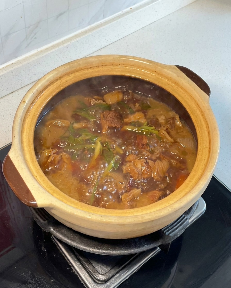Chopped potatoes and carrots mixed into the simmering red-braised beef inside a clay pot.