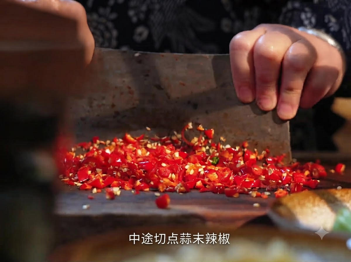 Fresh red chili peppers being chopped on a wooden board with a cleaver.