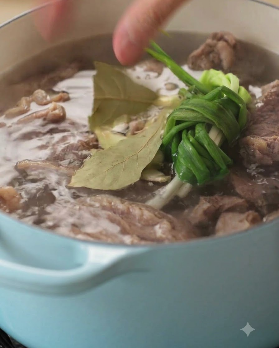 A close-up of aromatics and spices being dropped into a simmering pot of beef.