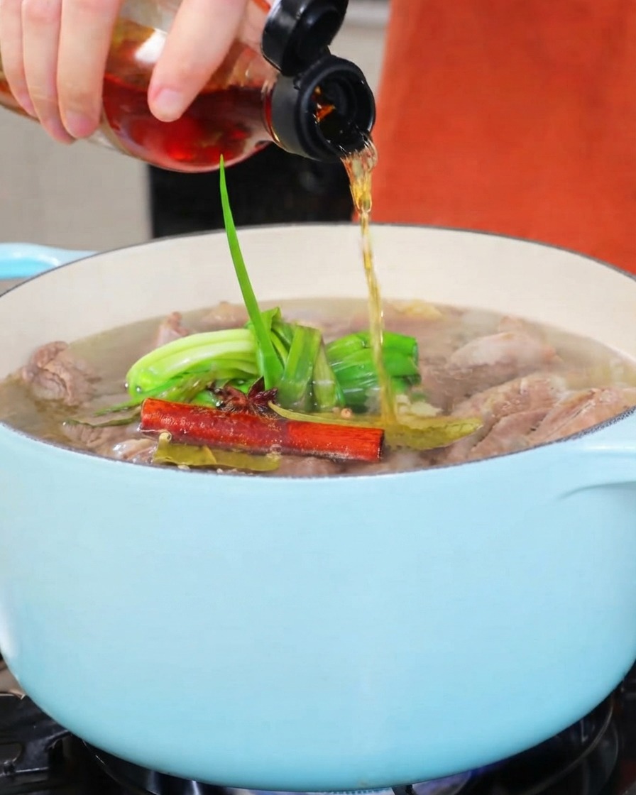 Cooking wine being poured from a small bottle into a light-colored stew pot.
