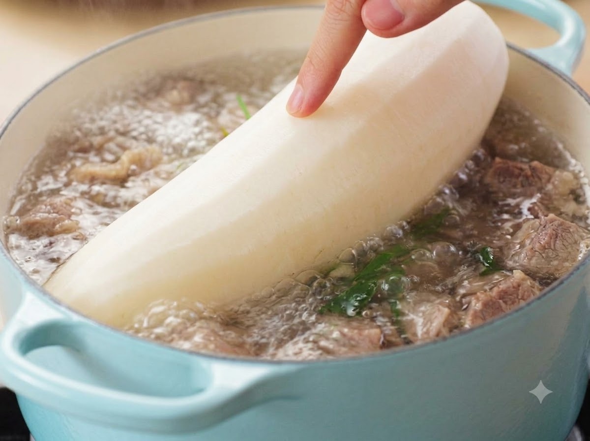A hand guiding a large peeled white radish into a bubbling pot of beef soup.