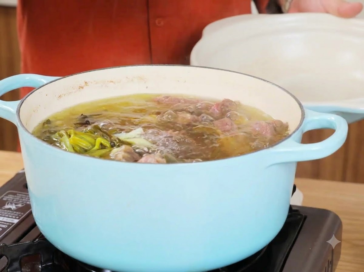 A pot of simmering beef broth after removing the main ingredients, showing clear liquid and green onions.