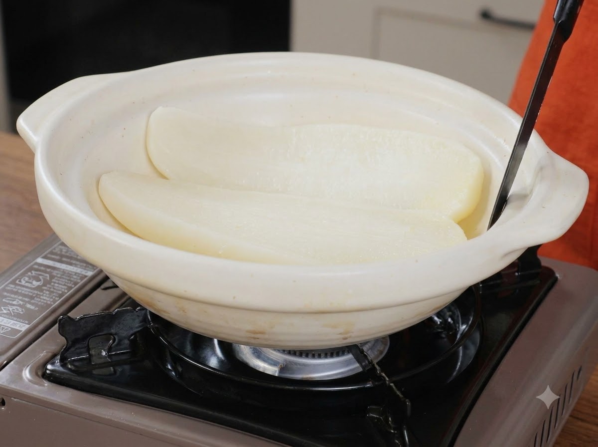 Two halves of cooked white radish resting inside a wide white ceramic serving pot with a utensil.