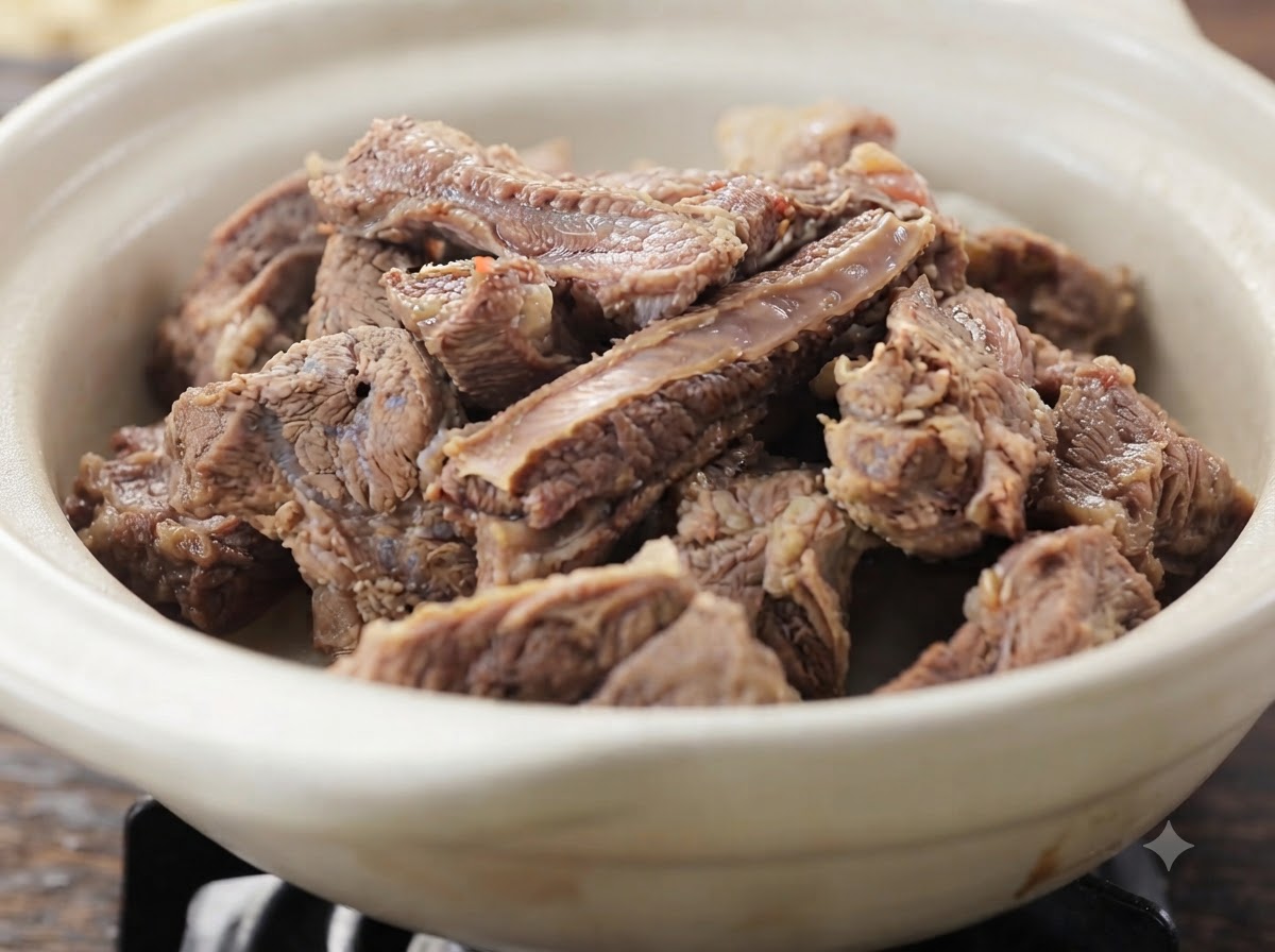A close-up view of tender cooked beef rib pieces piled inside a white ceramic dish.