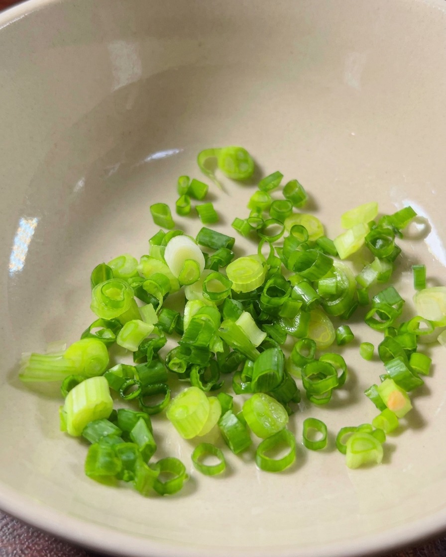 Finely minced garlic and fresh red millet chili slices placed inside a clean ceramic bowl.