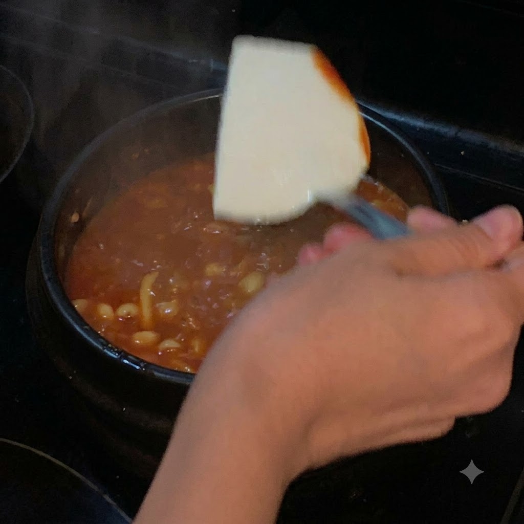 A slice of soft tofu being lowered with a spatula into a pot of red simmering soup.