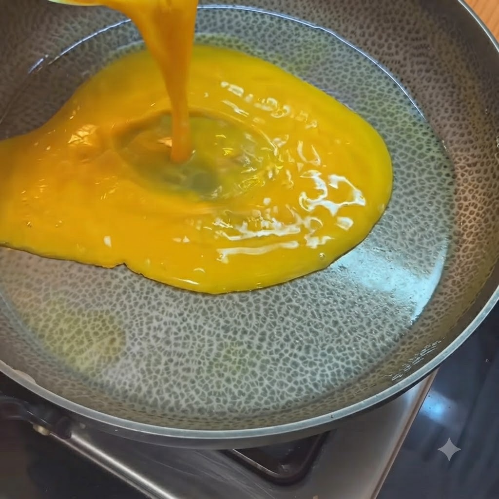 Bright yellow beaten eggs being poured from a measuring cup into a hot oiled pan.