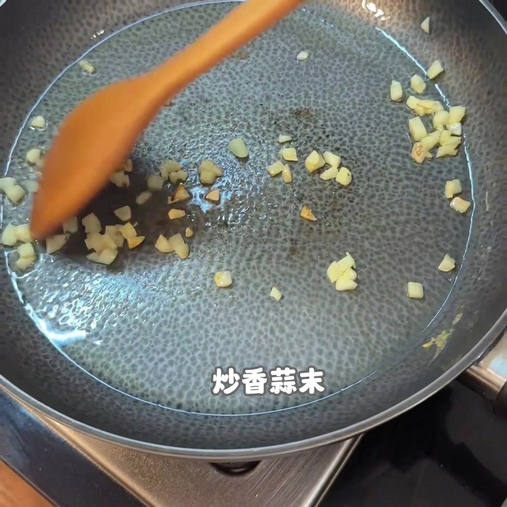 Chopped garlic and bits of food being stirred with an orange wooden spatula in a non-stick pan.