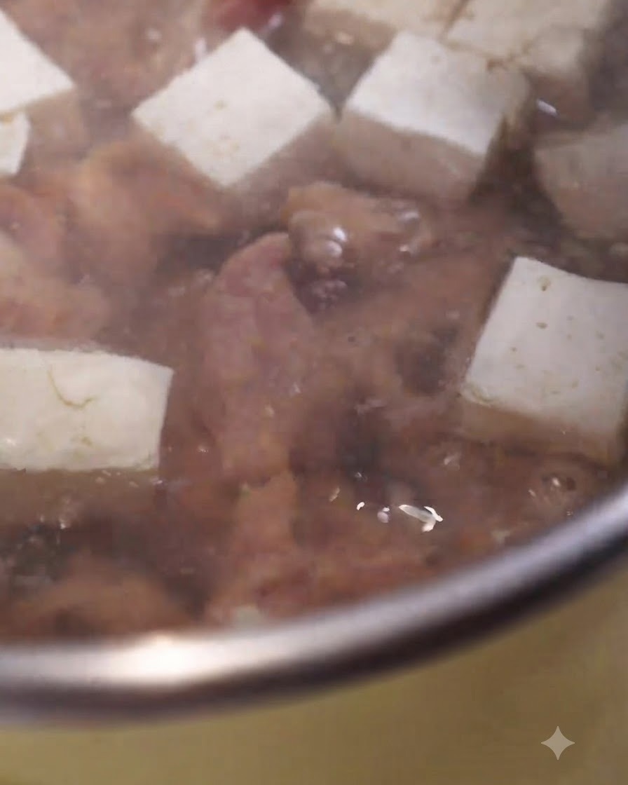 Marinated pork slices cooking in a bubbling pot of soup alongside cubes of white tofu.